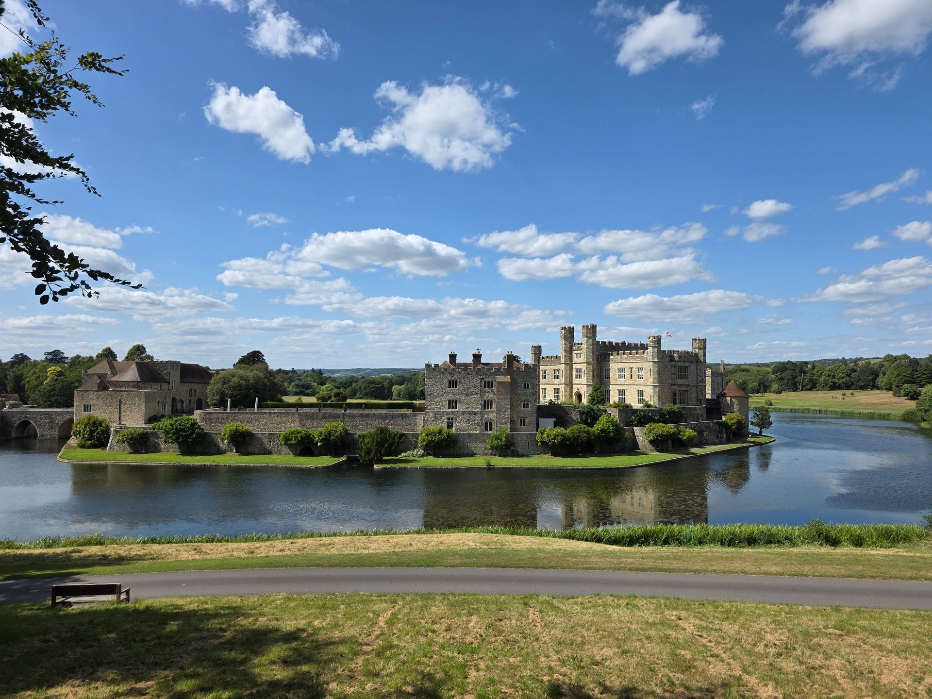 Leeds Castle on a lake under a blue sky, surrounded by greenery.