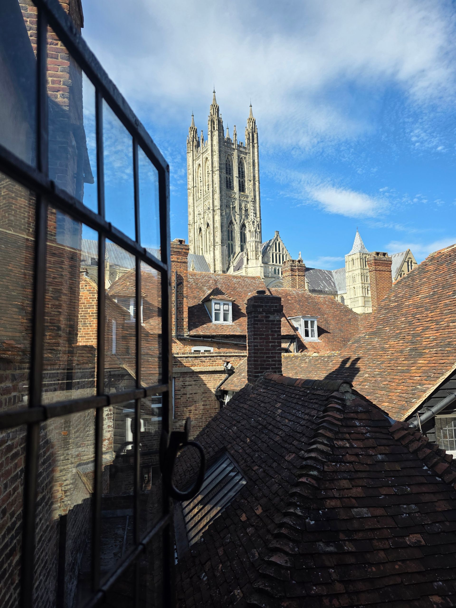 View from an open window of a gothic cathedral, the rooftops and blue sky are visible.