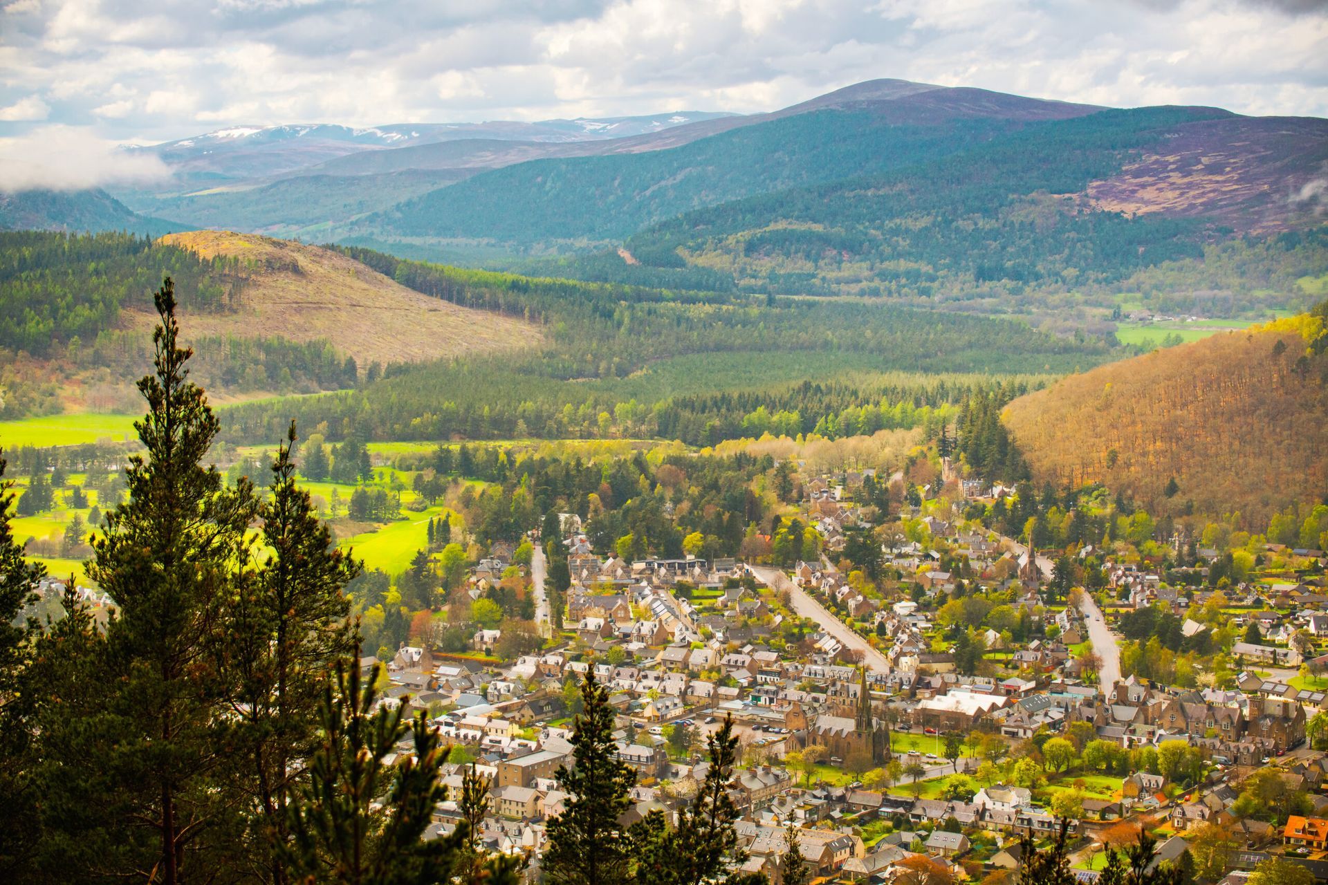 View of a village nestled in a valley, surrounded by green trees and hills.
