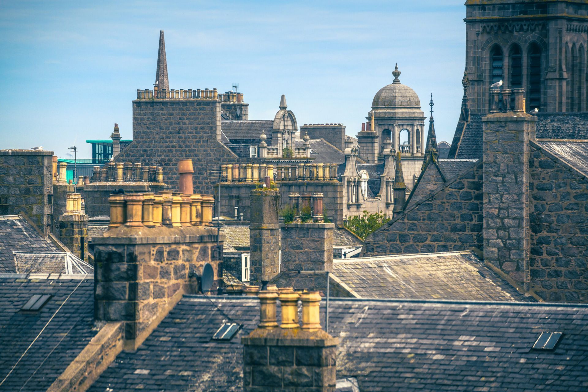 Roofs of stone buildings in Aberdeen, Scotland, with chimneys and a clear blue sky.