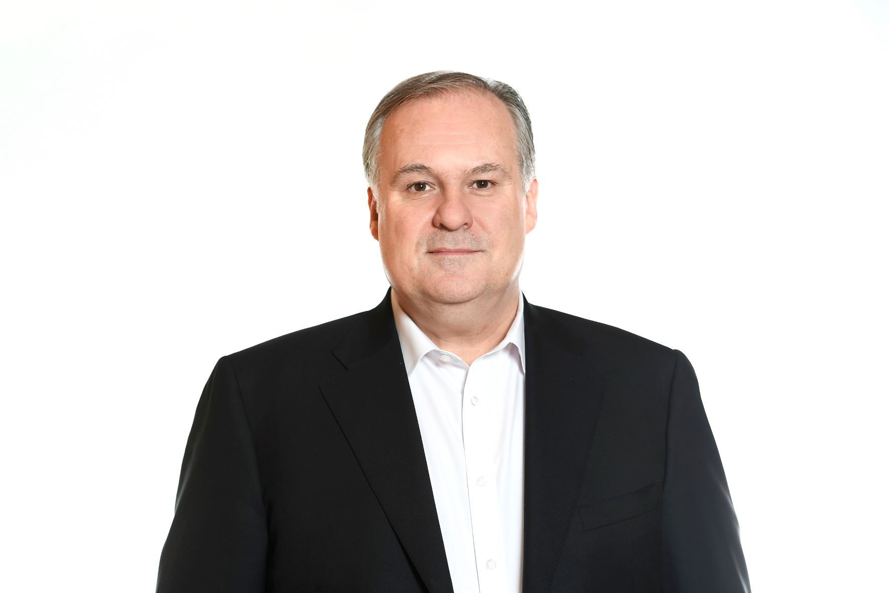 Man in a black suit jacket and white shirt, looking forward against a white backdrop.