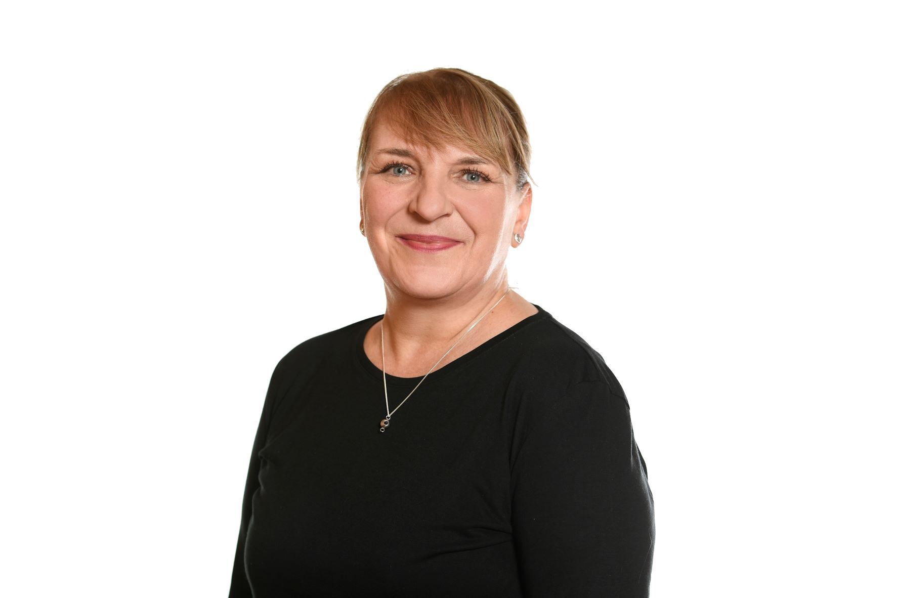 Woman with light skin wearing a black shirt, smiling against a white backdrop.