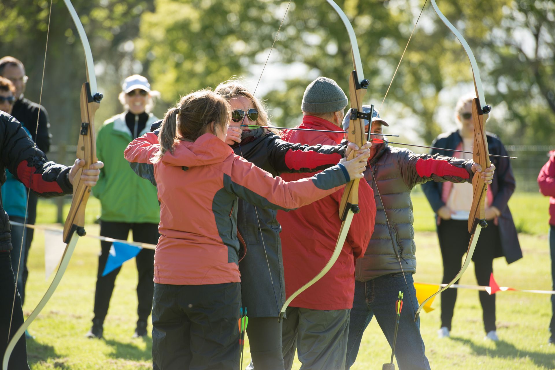 People practicing archery outdoors, aiming bows. Instructor assists archer.