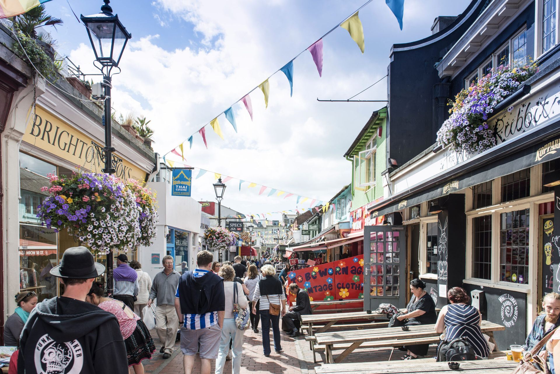 Crowded street in Brighton with shops, people, colorful bunting, and outdoor seating on a sunny day.