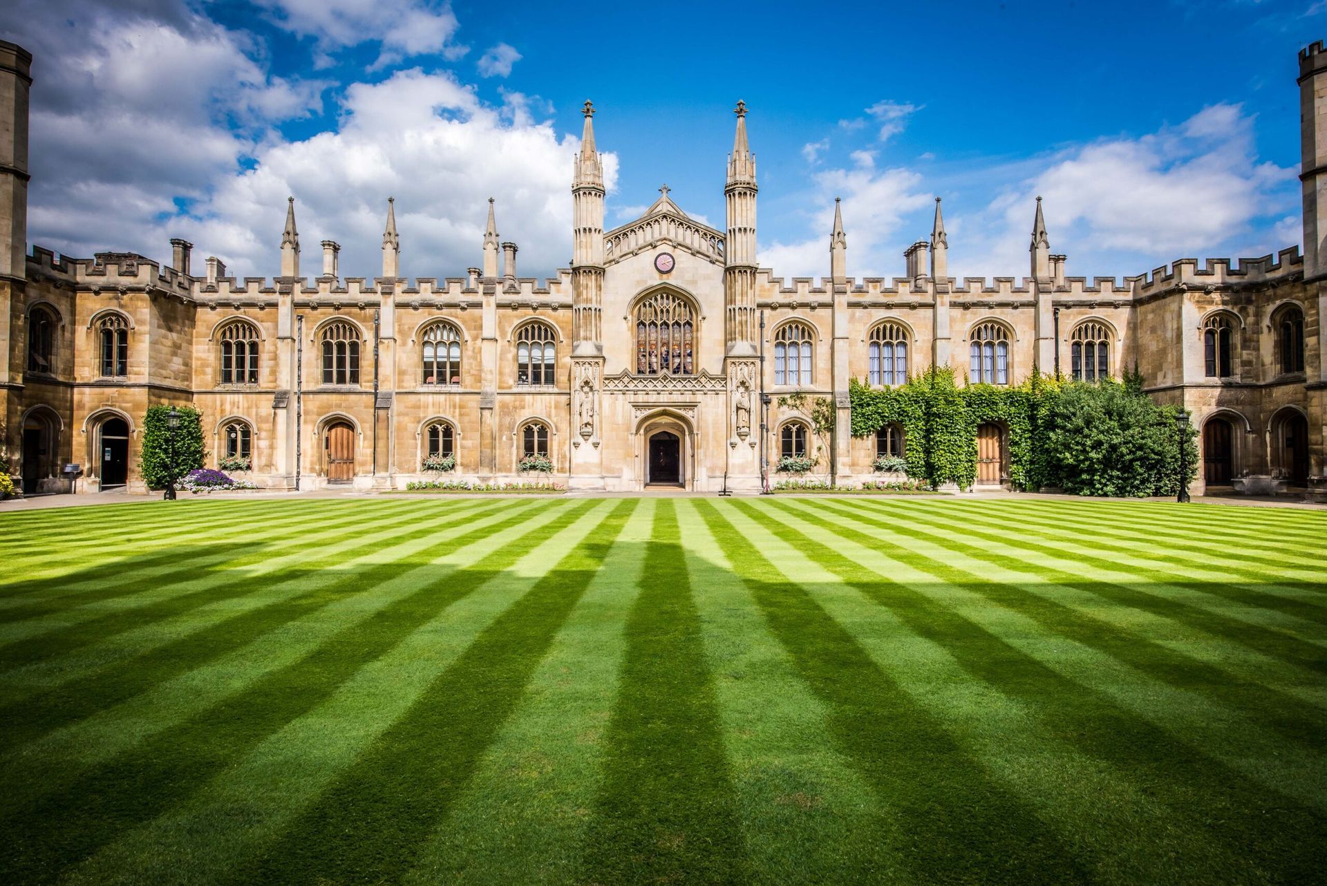 Lawn with striped patterns in front of a large, ornate stone building under a blue sky in Cambridge.