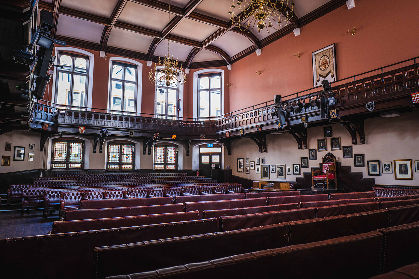 Auditorium with red leather seating, balcony, windows, and ornate ceiling.