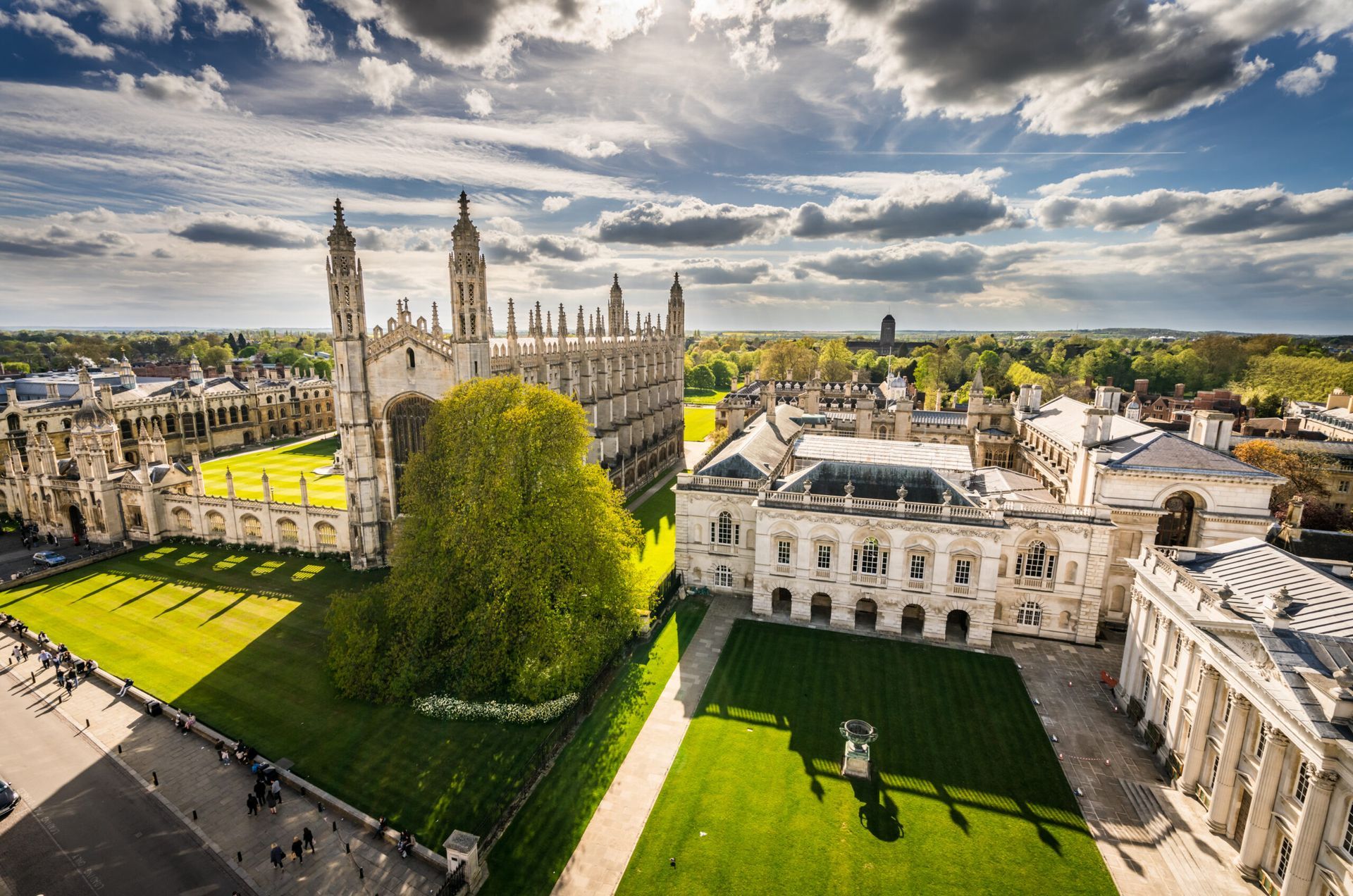 Aerial view of Cambridge University, with large stone buildings, green lawns, and a bright sky.