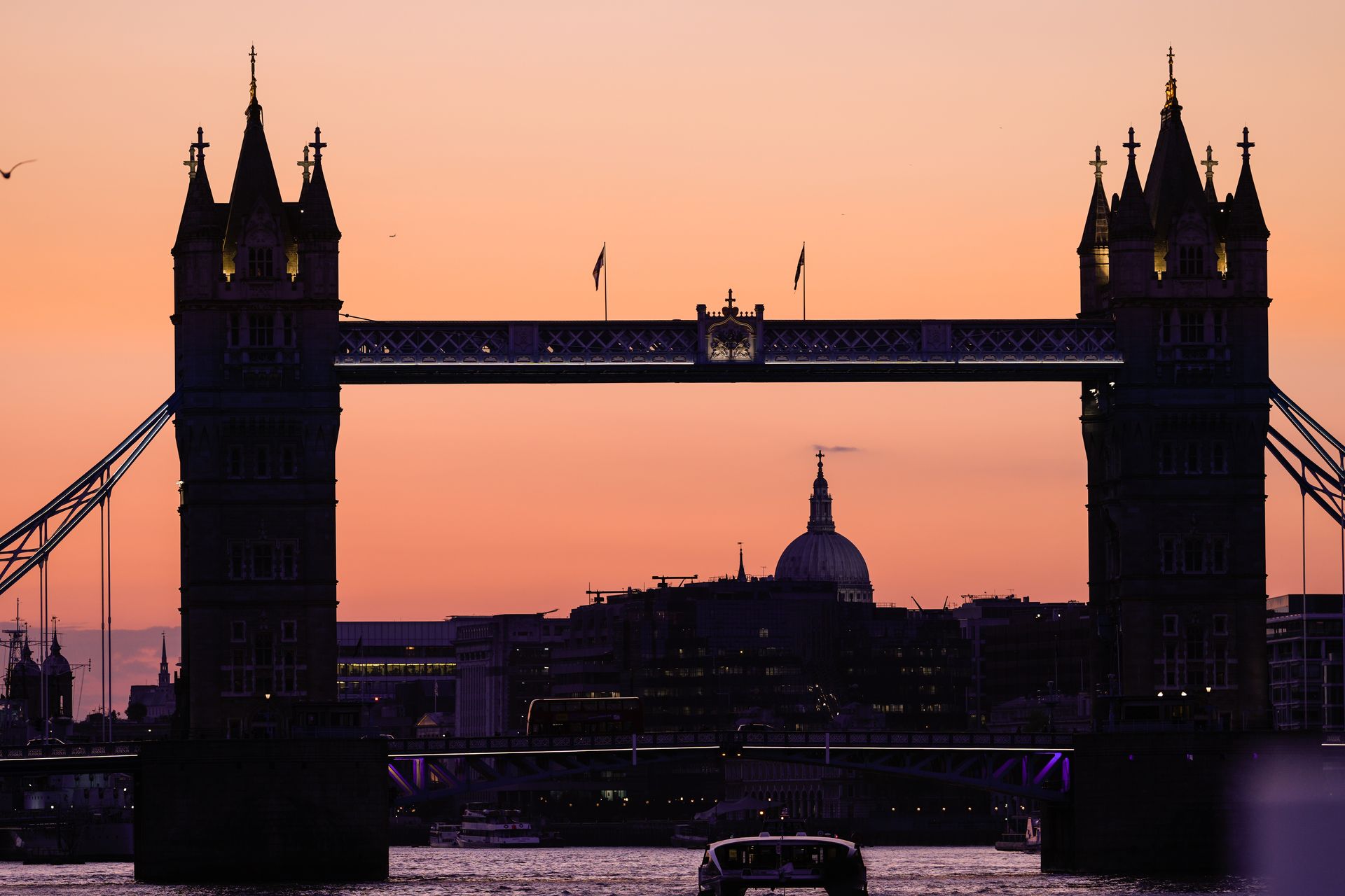 Tower Bridge silhouetted against an orange sunset; skyline with dome visible through the bridge.