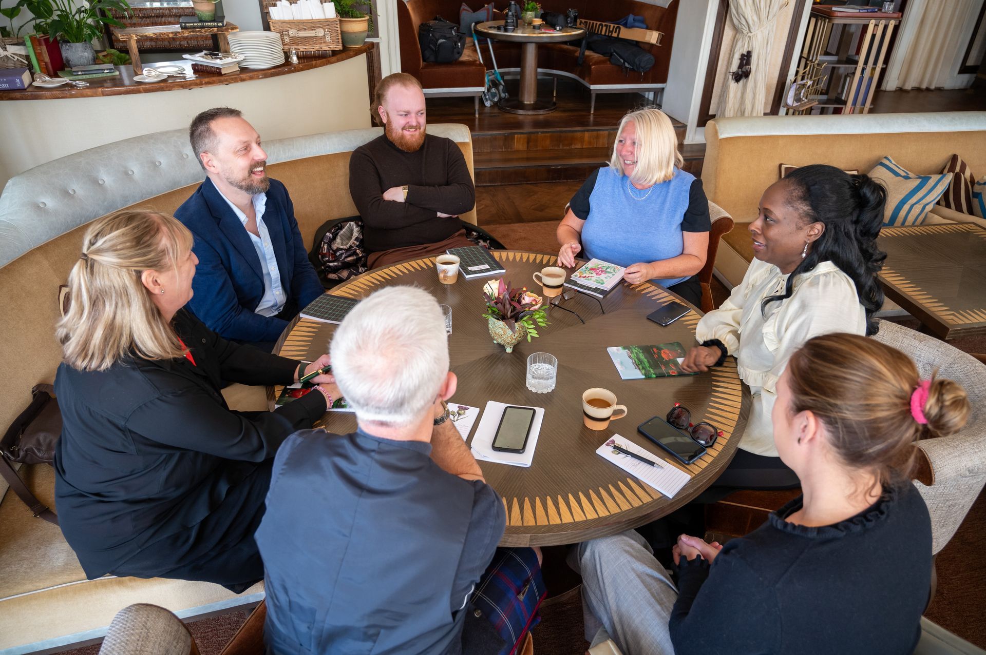 Group of people sitting around a round table in a cafe, engaged in a discussion.