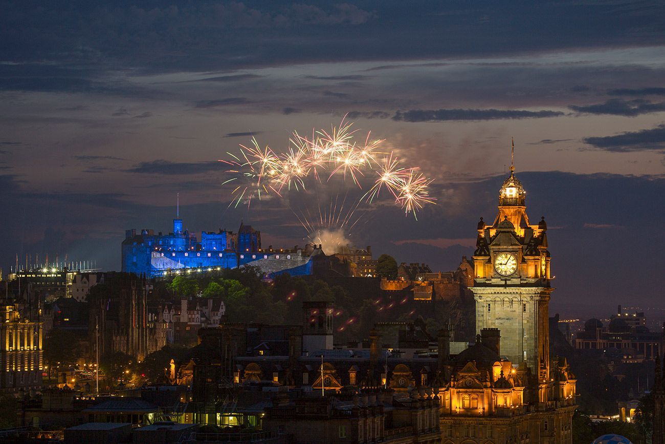 Fireworks over Edinburgh Castle and illuminated clock tower at dusk.