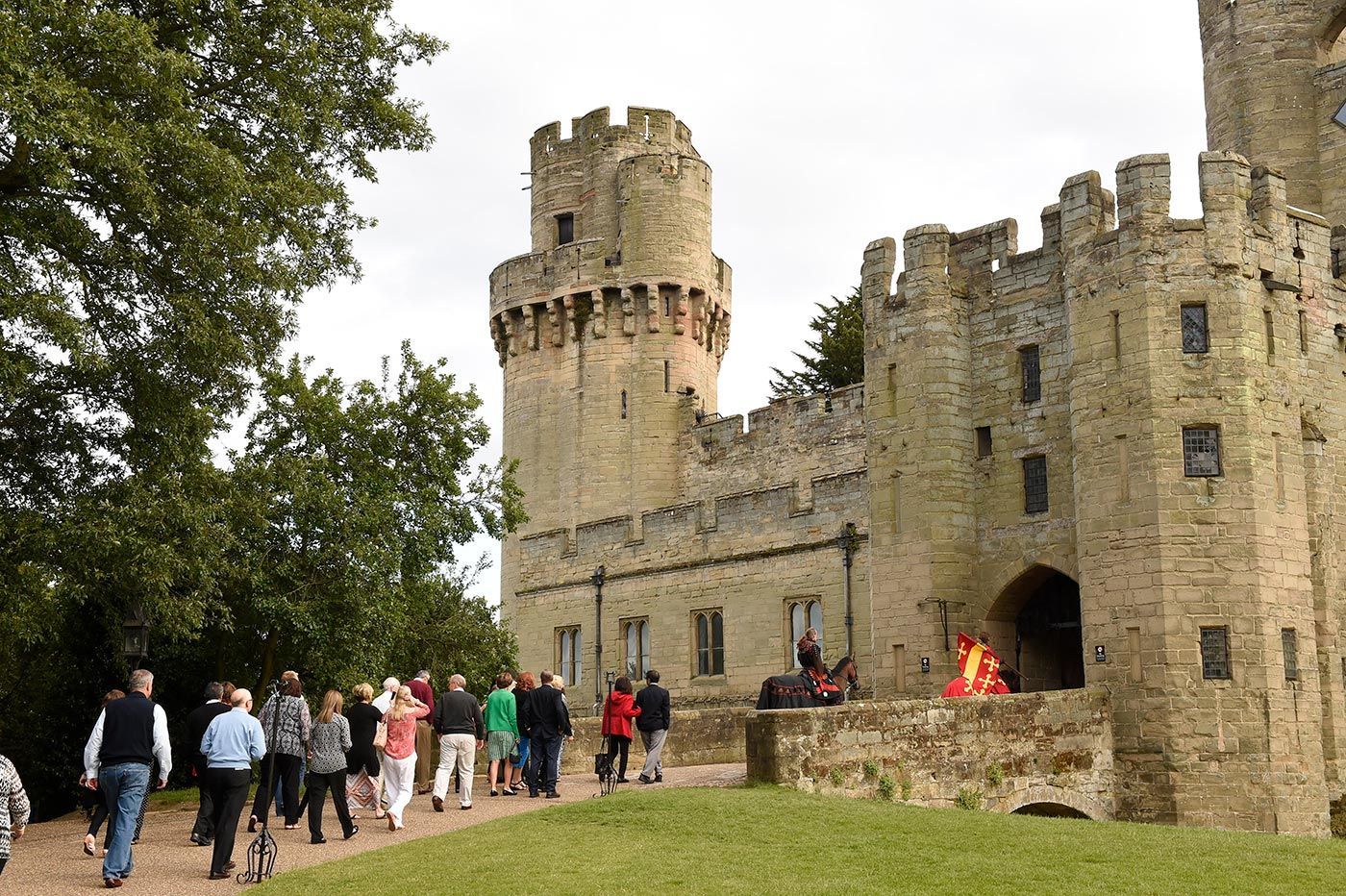 People walk toward a stone castle with a tower and entrance archway; fire burns.