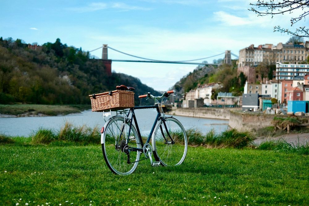 Bicycle with basket in front of Clifton Suspension Bridge, Bristol, UK, with river and buildings in background.