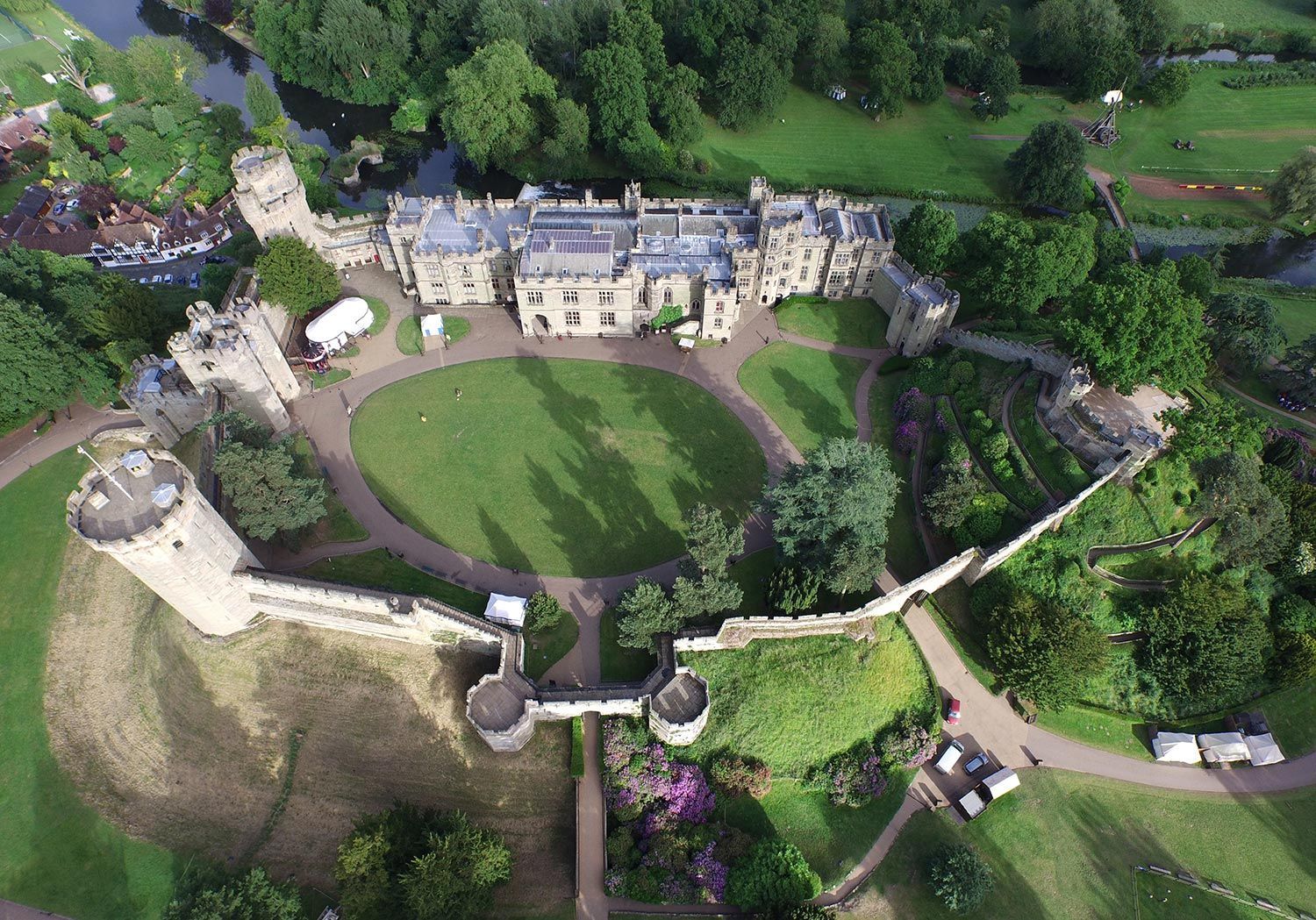 Aerial view of Warwick Castle, England, with stone walls, towers, and a green lawn.