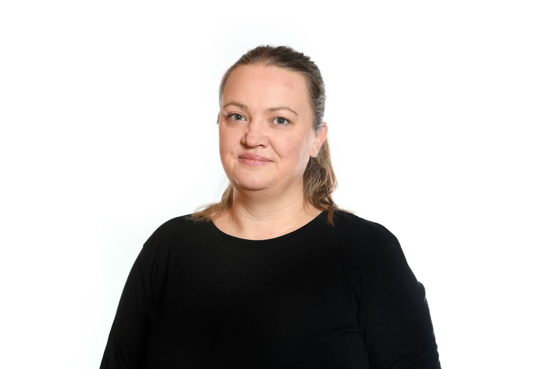 Woman with light skin, brown hair pulled back, wearing a black long-sleeved shirt, smiles. White background.