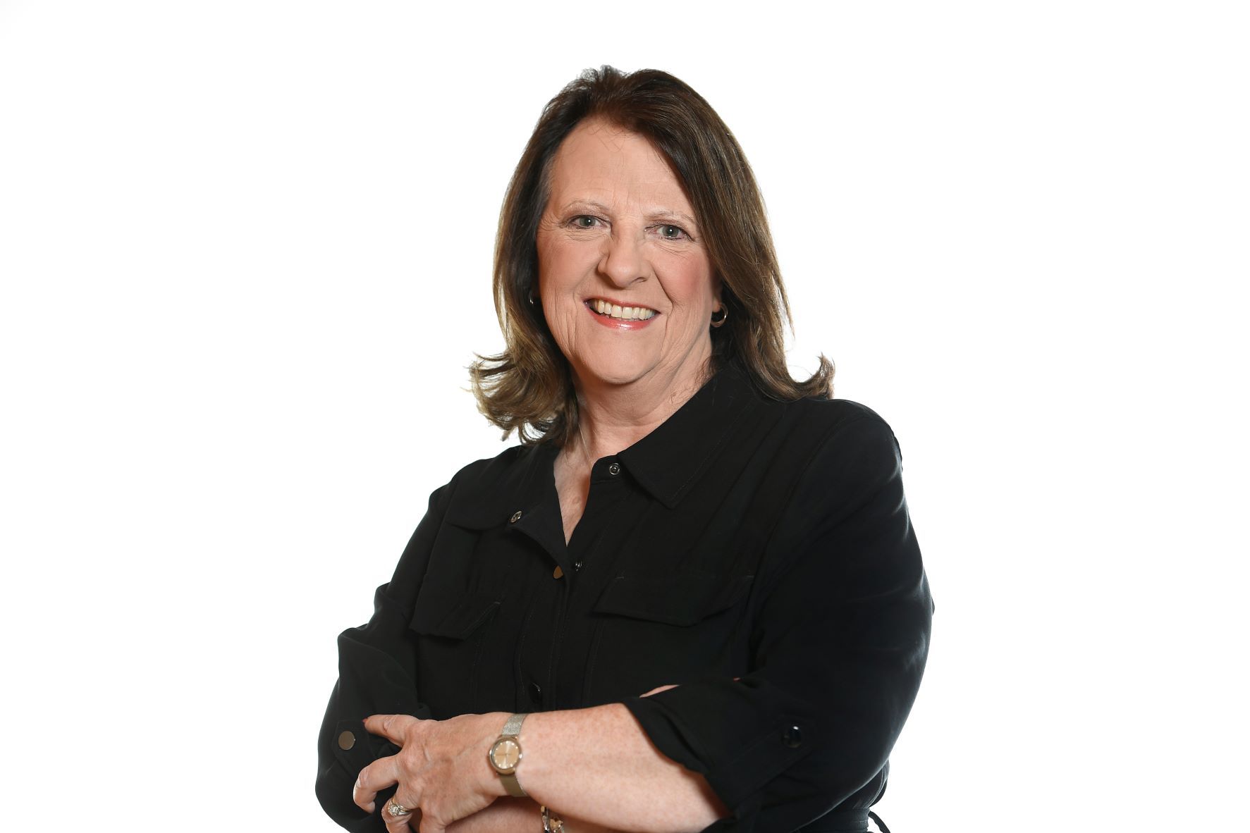 Woman with dark hair in a black button-up shirt smiles, arms crossed, set against a white backdrop.
