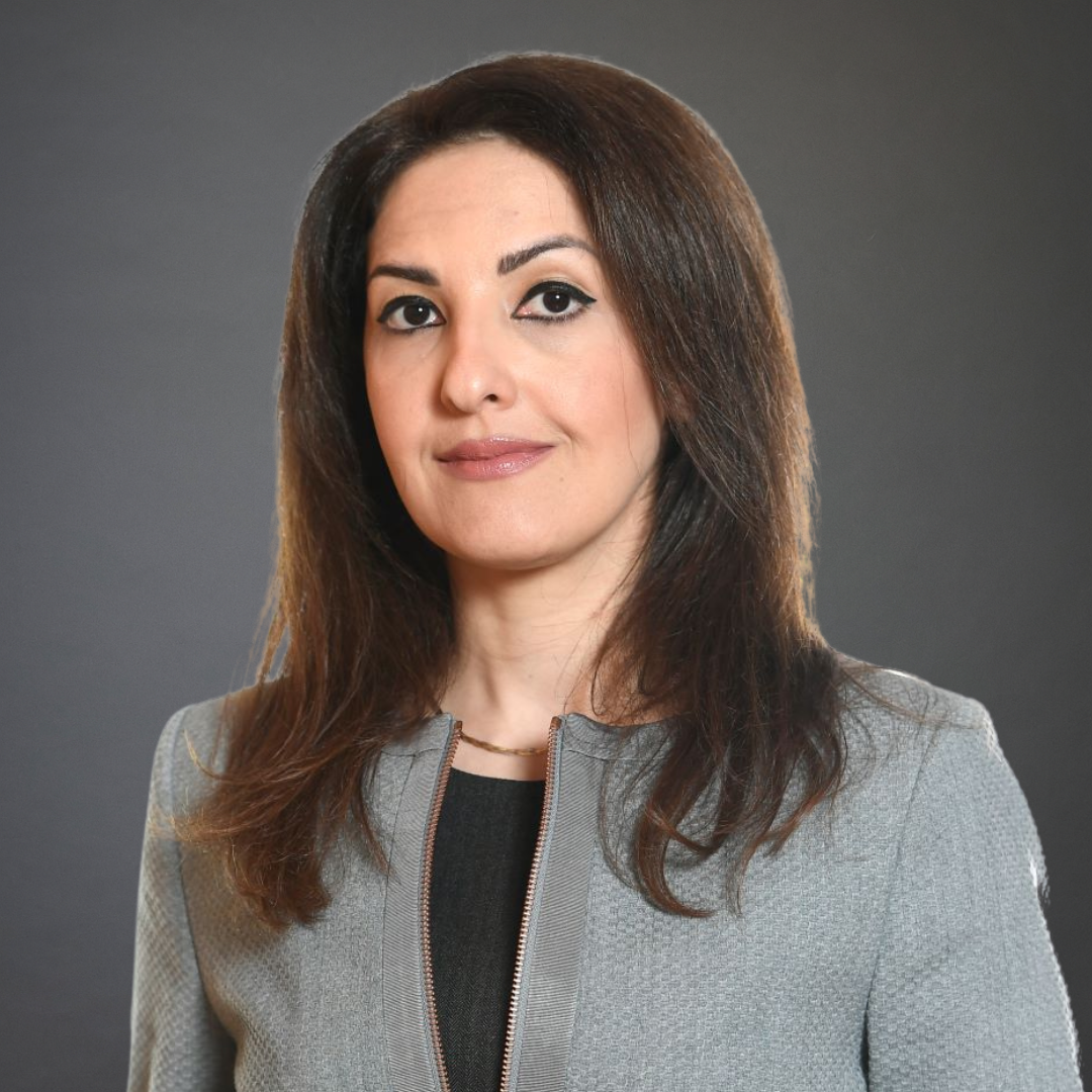 Woman with long brown hair, wearing a gray blazer, looking at the camera.
