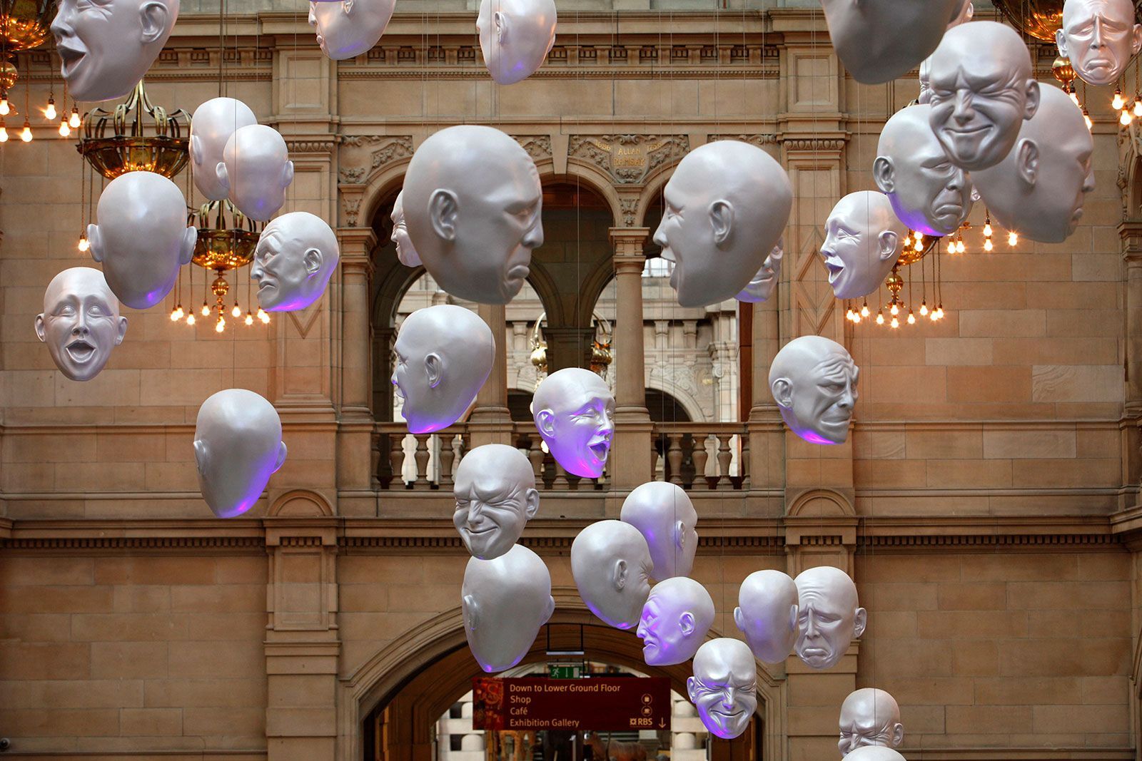 White sculpted heads, suspended in a grand hall, with various facial expressions and soft purple lighting.