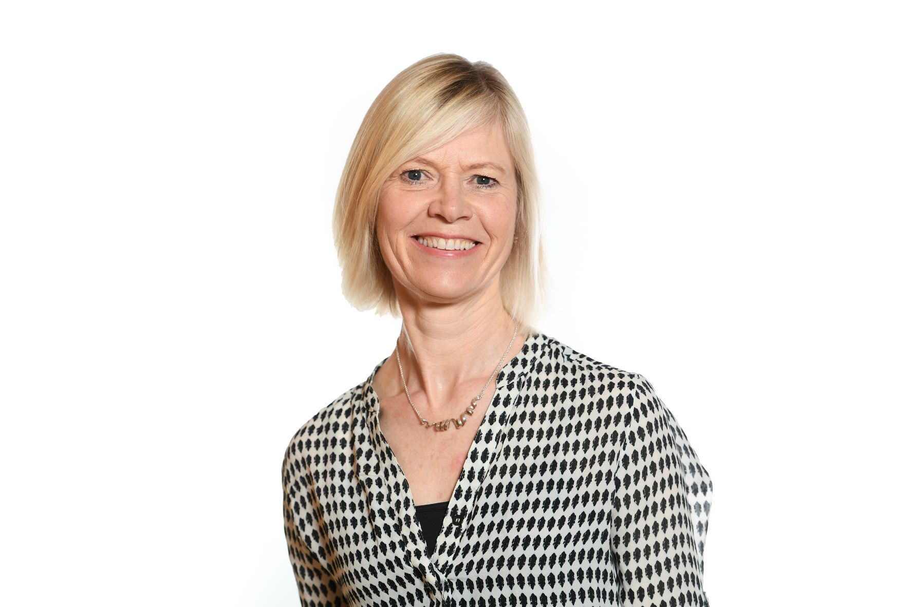 Woman with blonde hair wearing a black and white patterned shirt, smiling against a white background.
