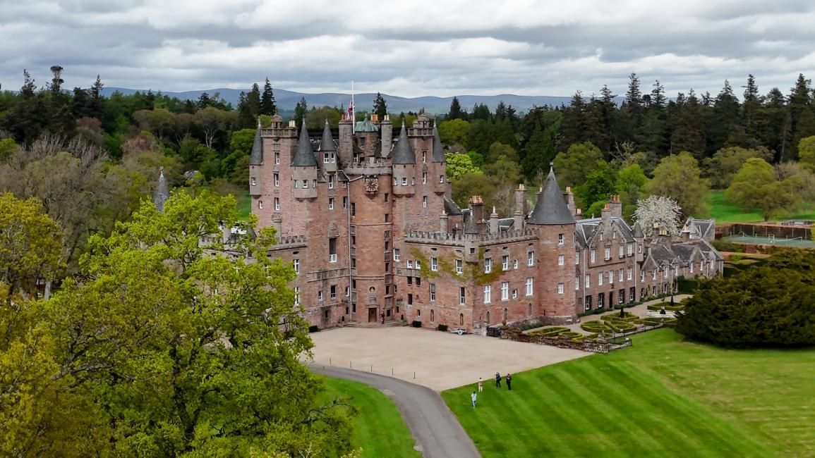 Aerial view of a large, old castle in Scotland, surrounded by trees and a long driveway.