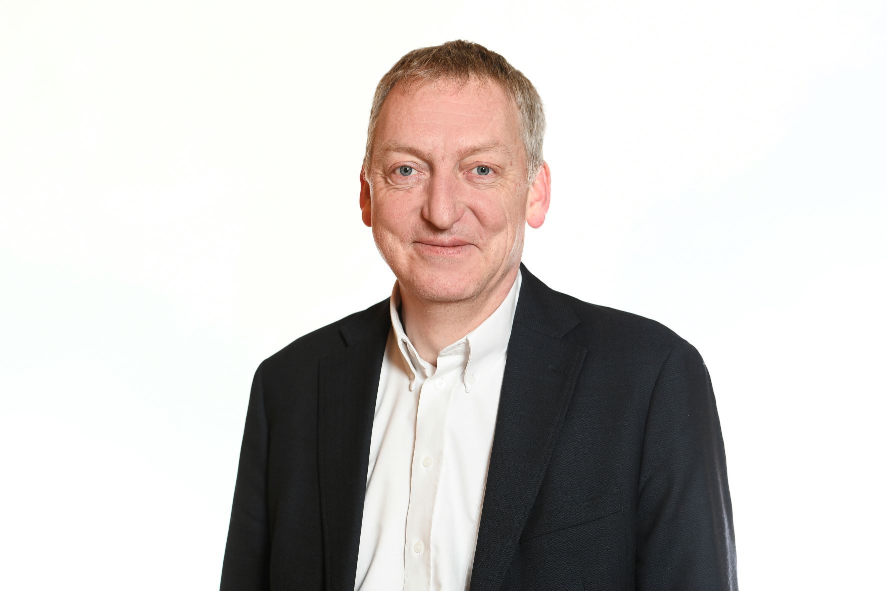 Man in a black blazer and white shirt, smiling against a white background.