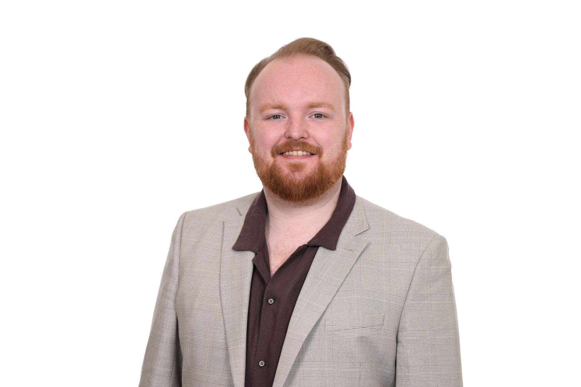 Man with red beard, wearing a tan blazer over a brown shirt, smiling.