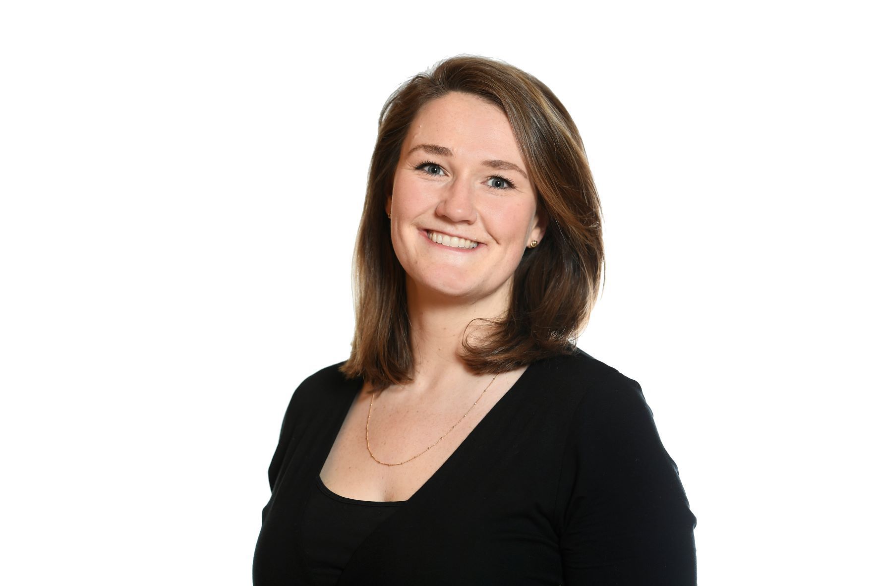 Woman with brown hair smiling, wearing a black top against a white background.