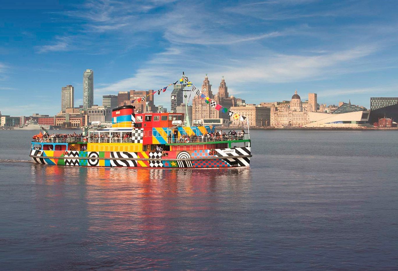 Colorful ferry boat on water with city skyline in the background.