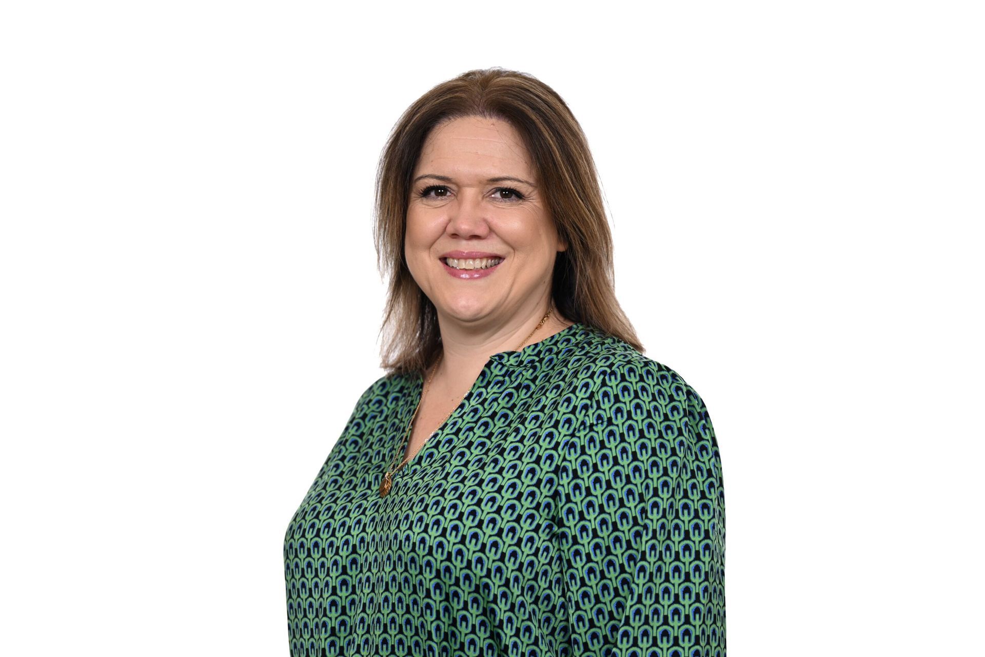 Woman with shoulder-length brown hair, wearing a green patterned blouse, smiles at the camera against a white background.