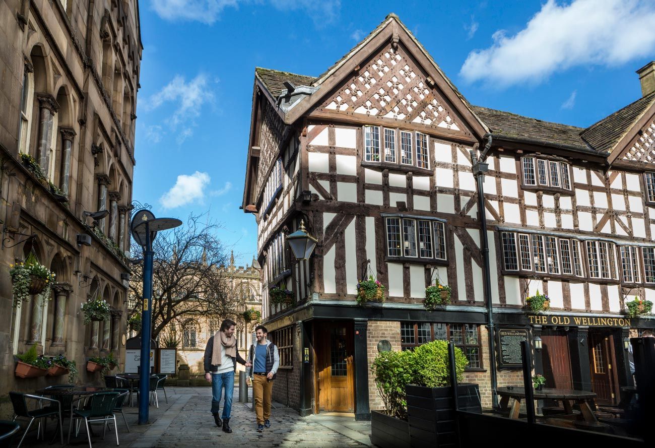 Two people walk on a cobblestone street. Tudor-style building with white and dark wood facade. Sunny day.