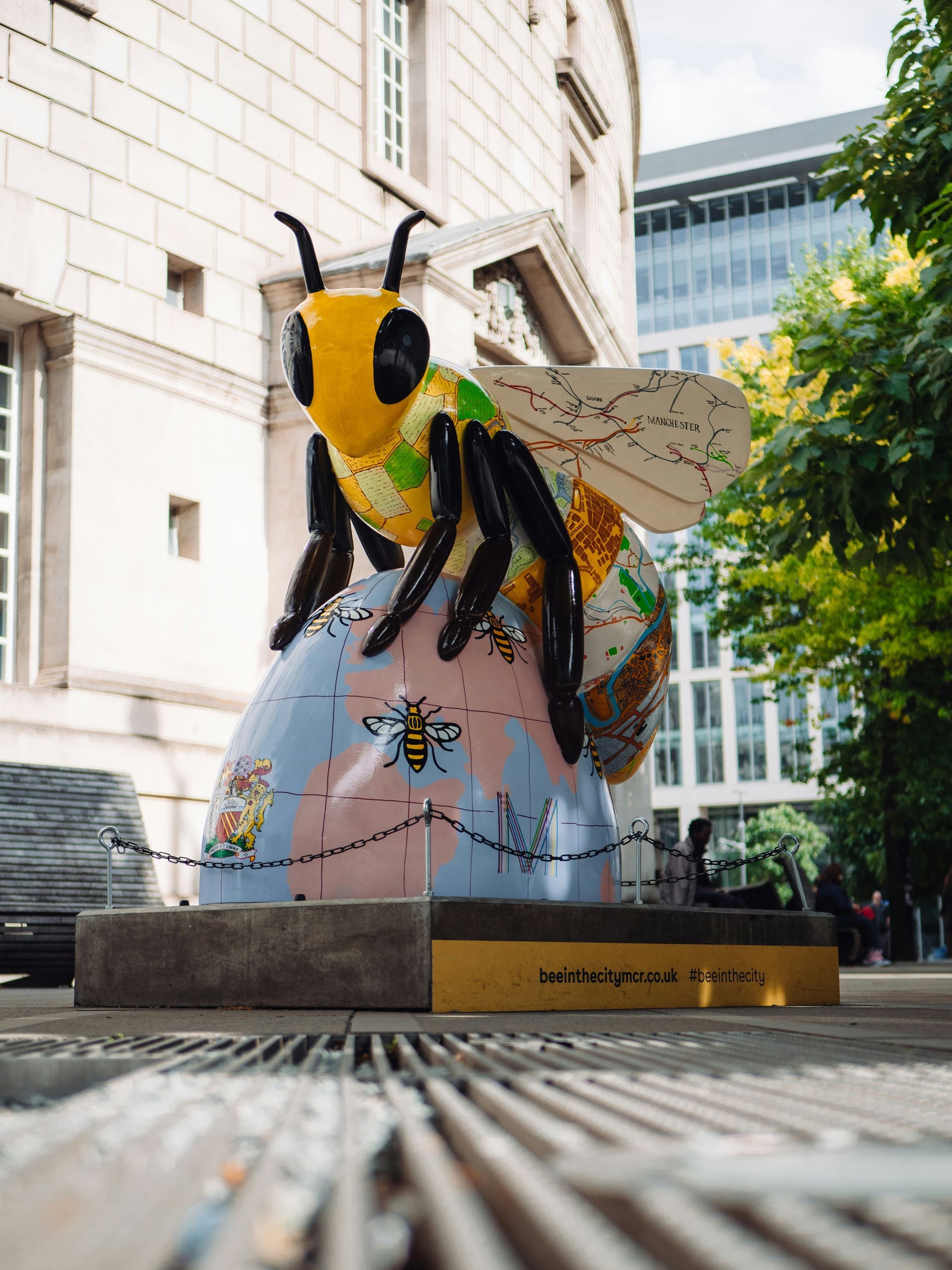 Giant colorful bee statue perched atop a globe with a building in the background.