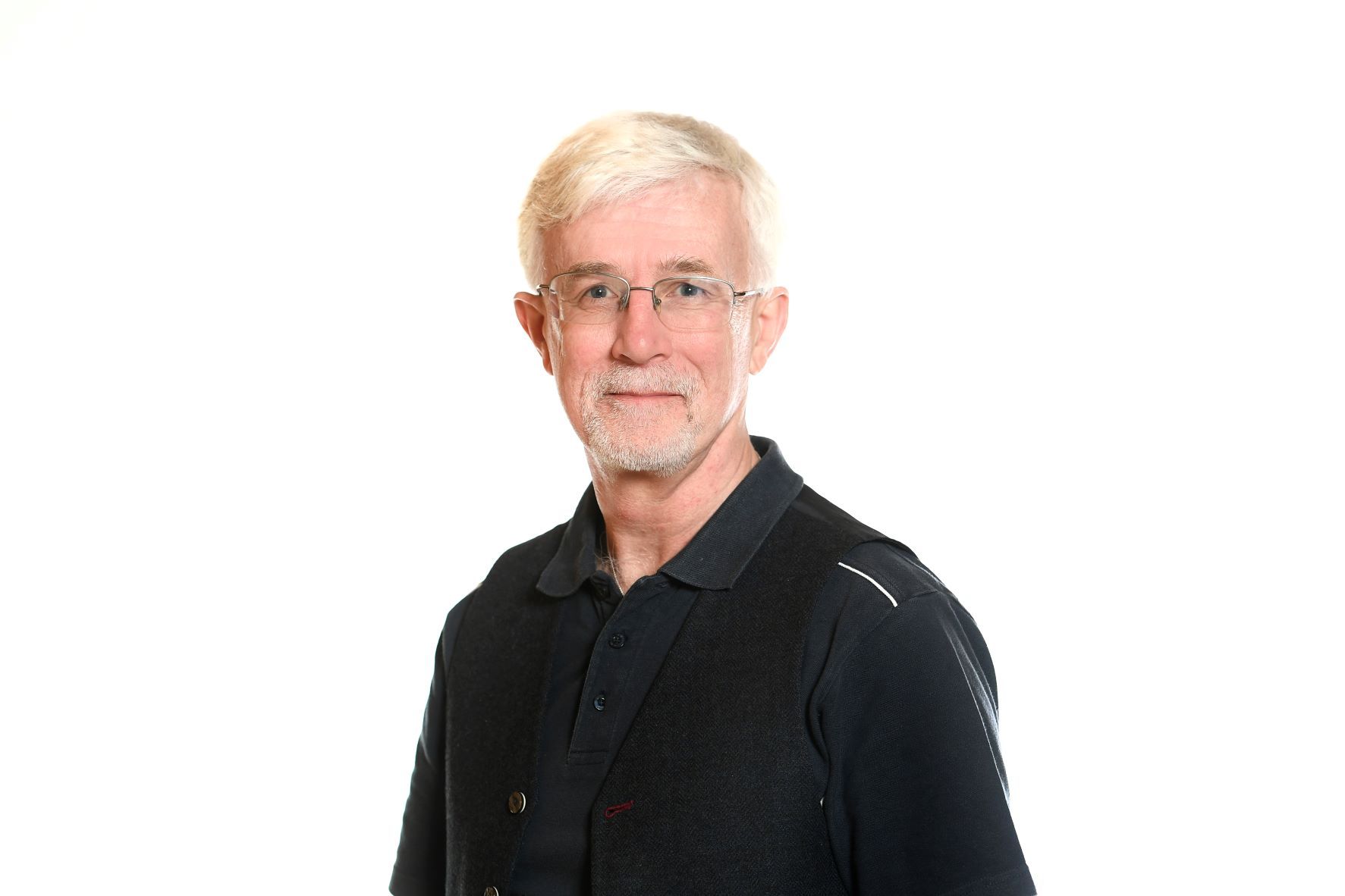 Man with gray hair and beard, wearing glasses and black top, smiling.