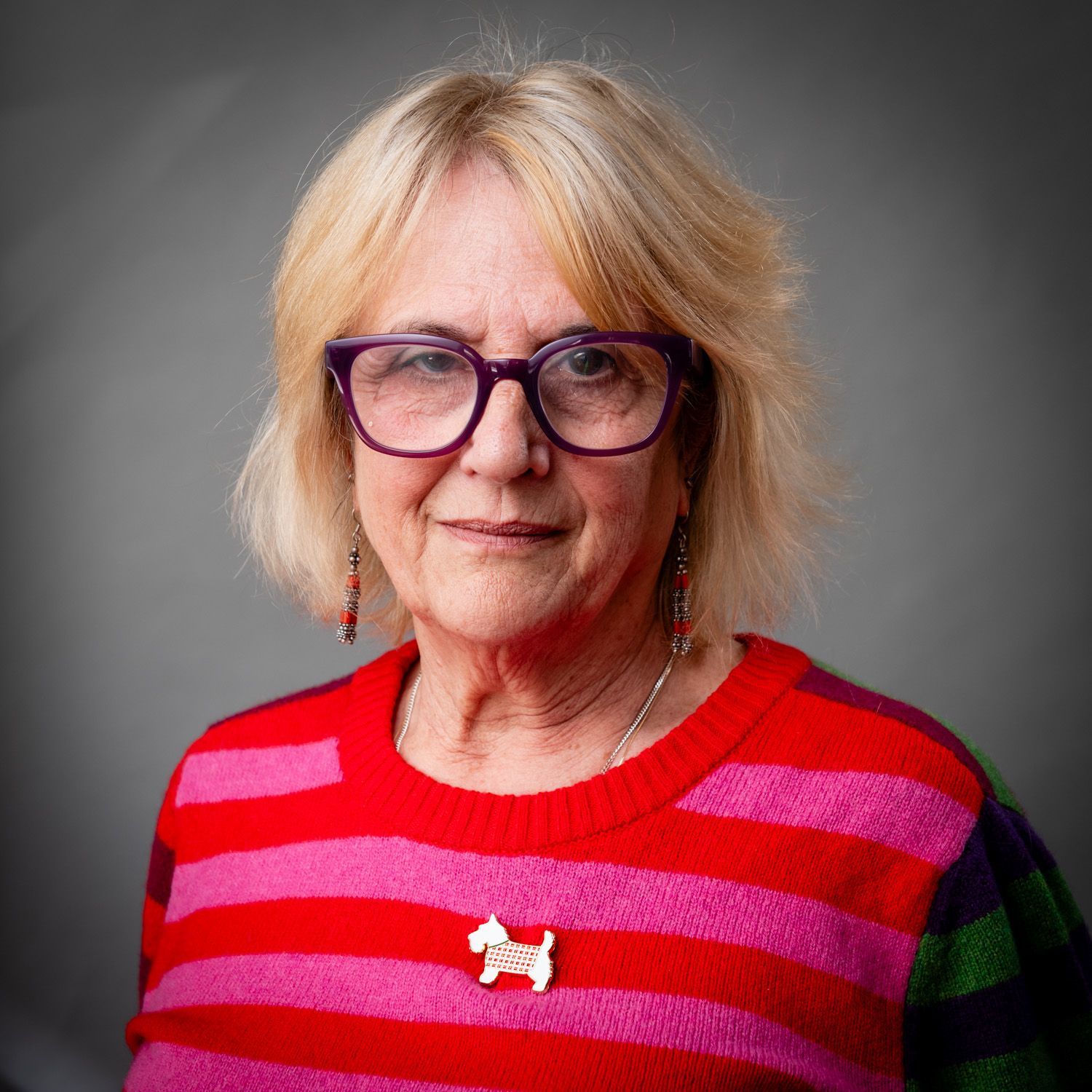 Woman with glasses and colorful striped sweater, smiling.