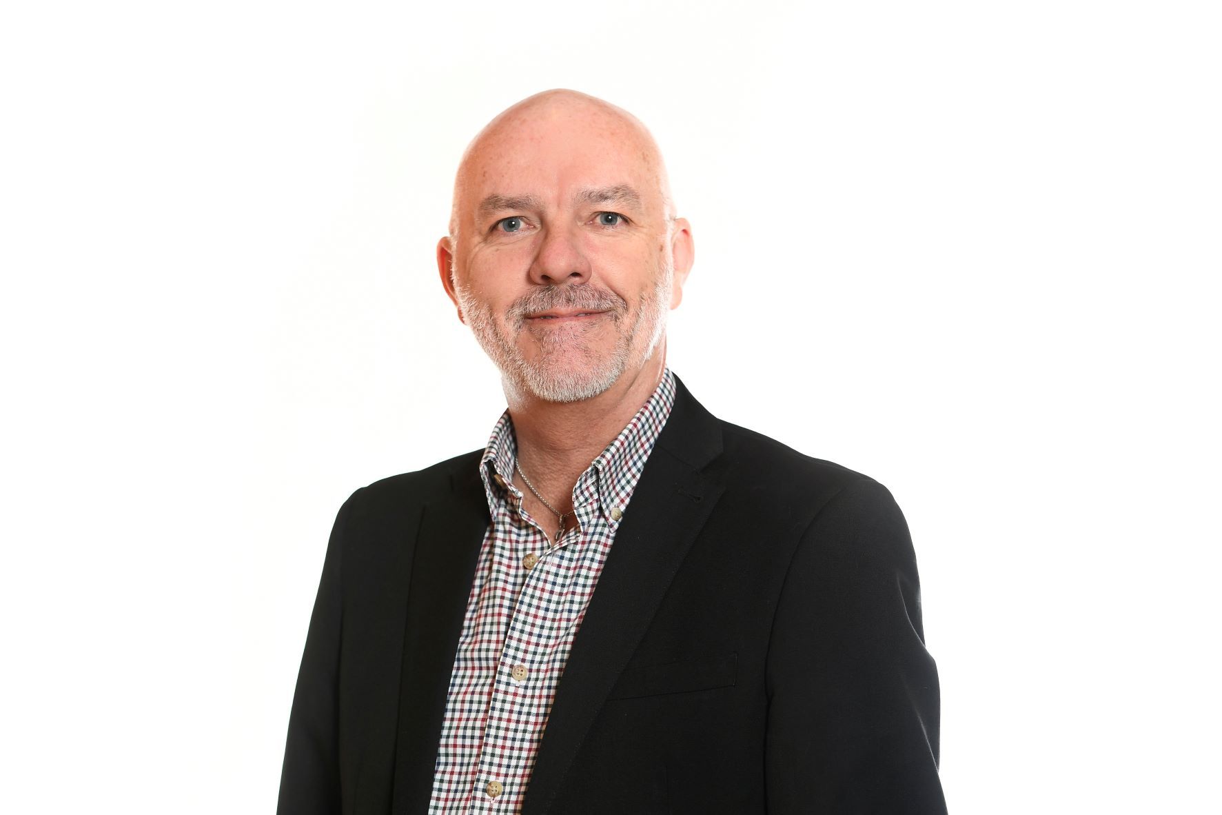 Man in black blazer and button-down shirt smiles, standing against a white backdrop.