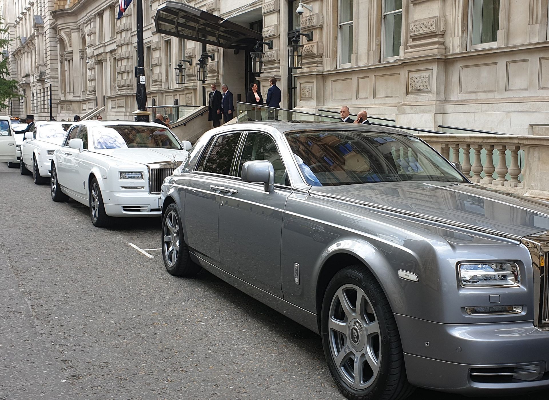 Row of Rolls-Royce cars parked outside a building with people near the entrance.
