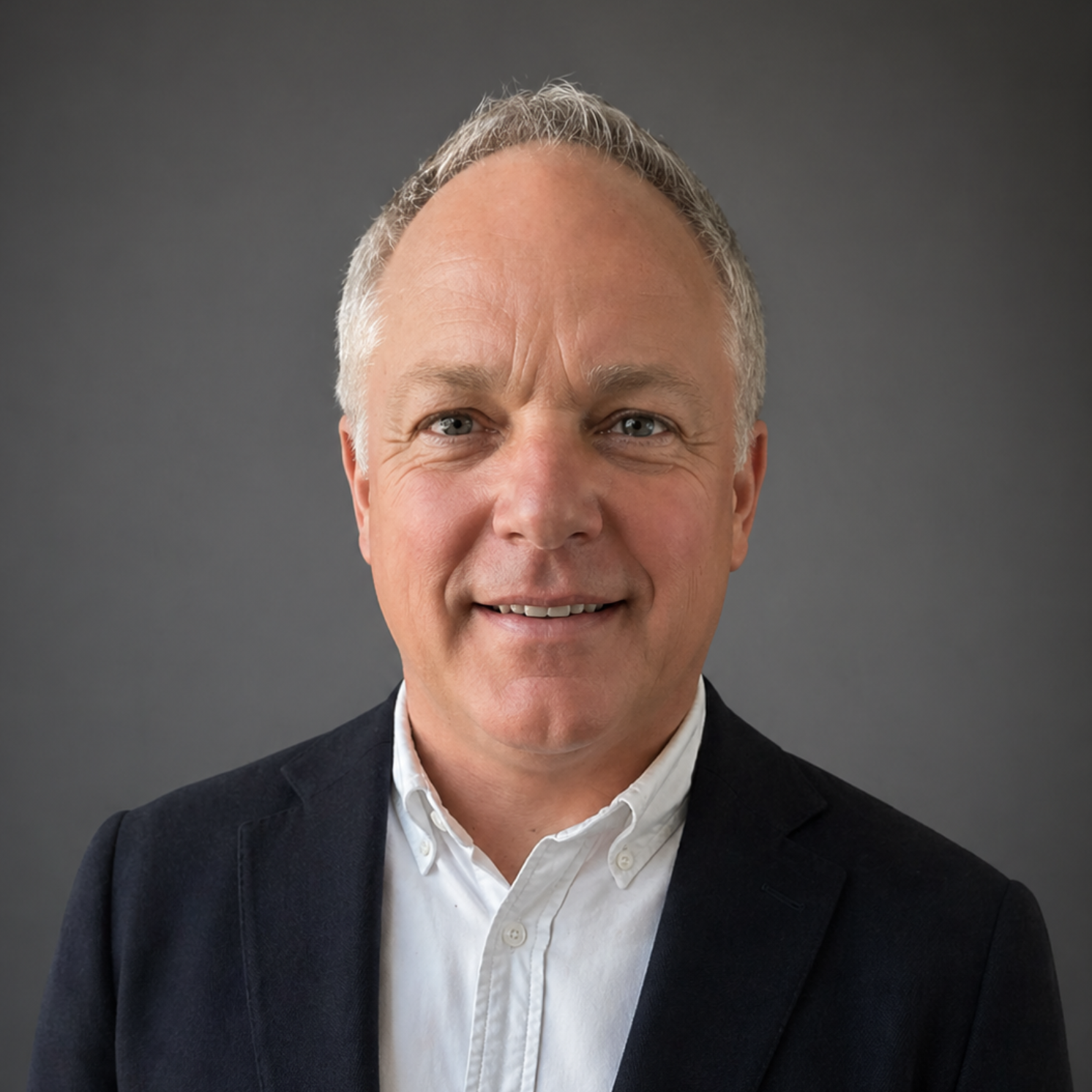 Smiling man in a dark blazer and white shirt against a gray background