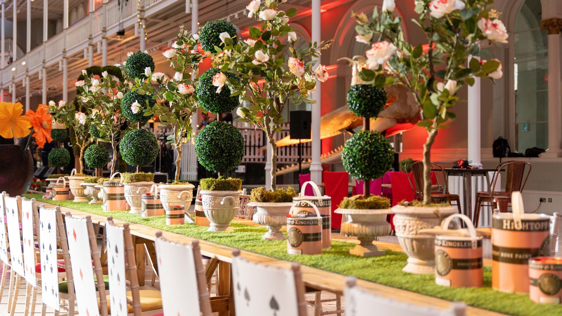 Long table set with floral arrangements and greenery in a white-walled venue.
