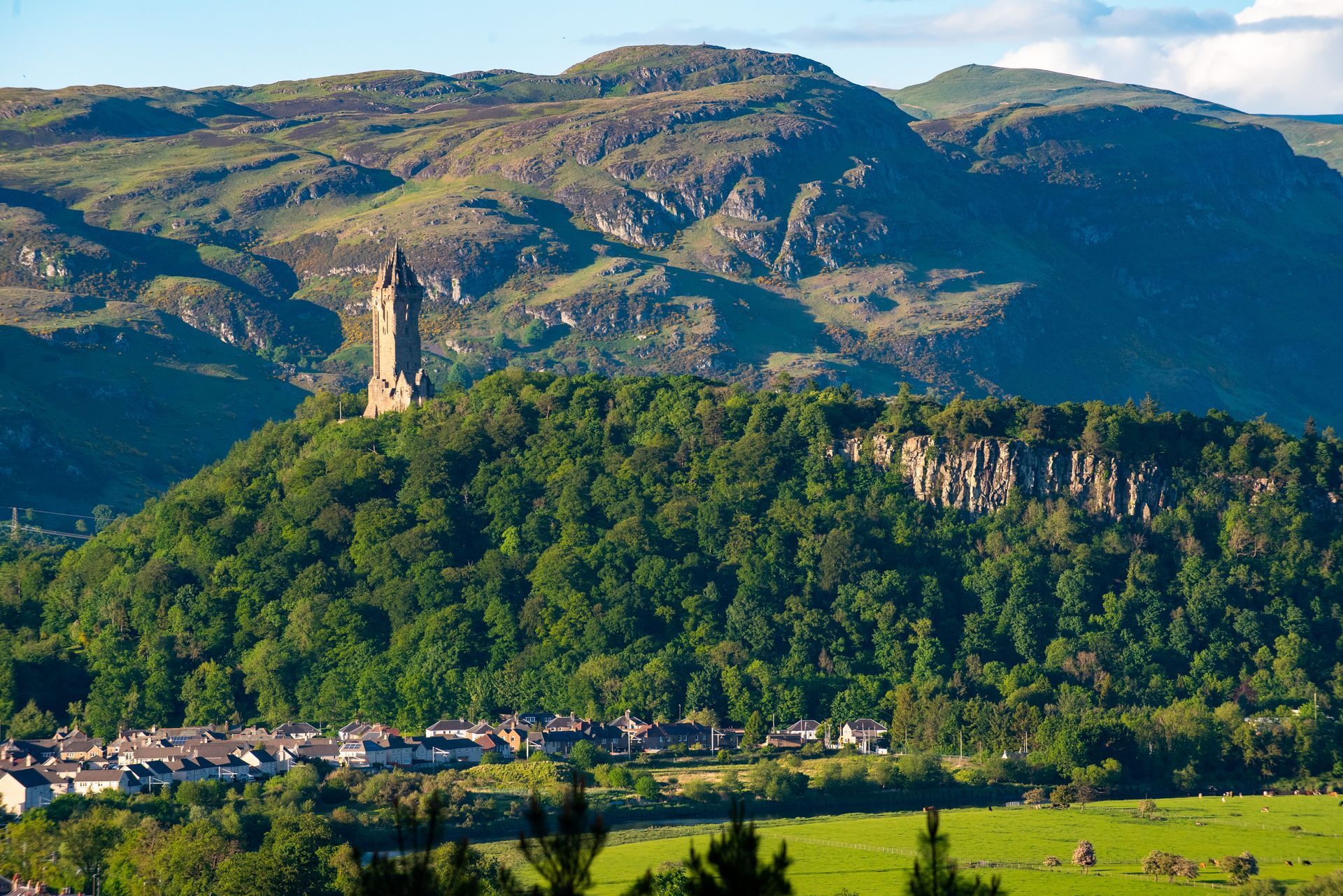 The Wallace Monument atop a forested hill in Stirling, Scotland, with a town in the foreground.