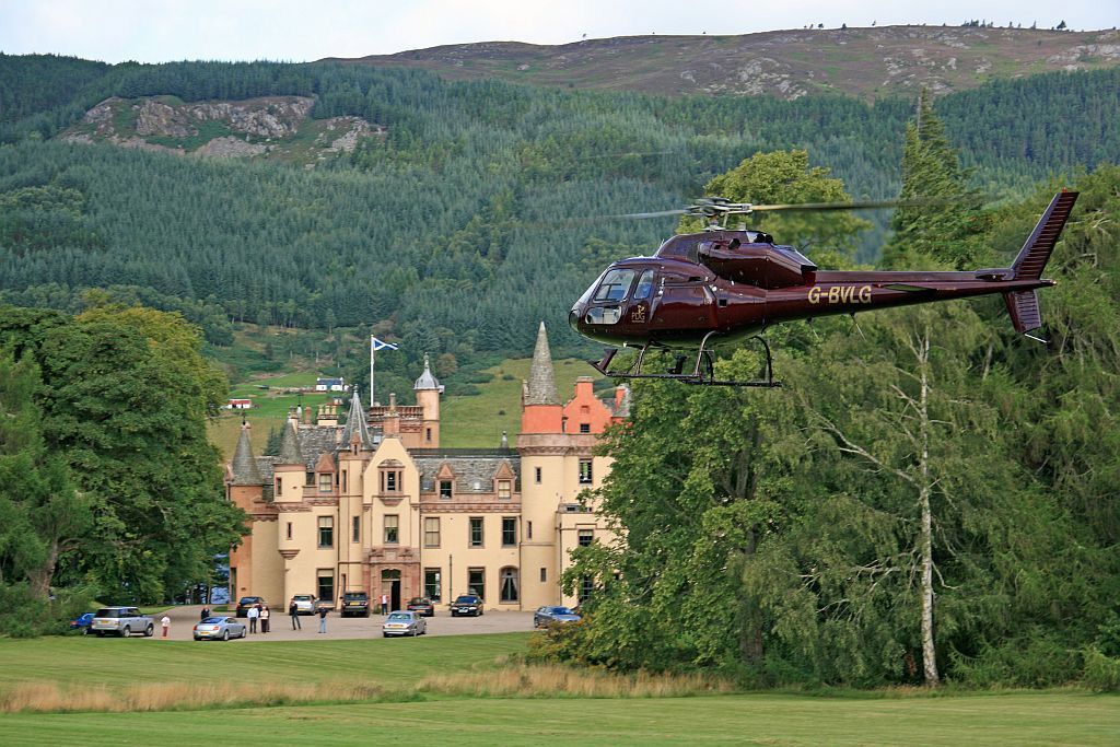 Helicopter flying past a large castle with a forested hill in the background.