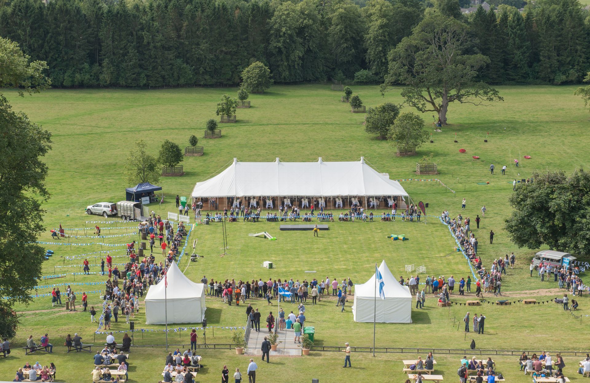 Large white tent in a green field with many people gathered; smaller white tents in the foreground.