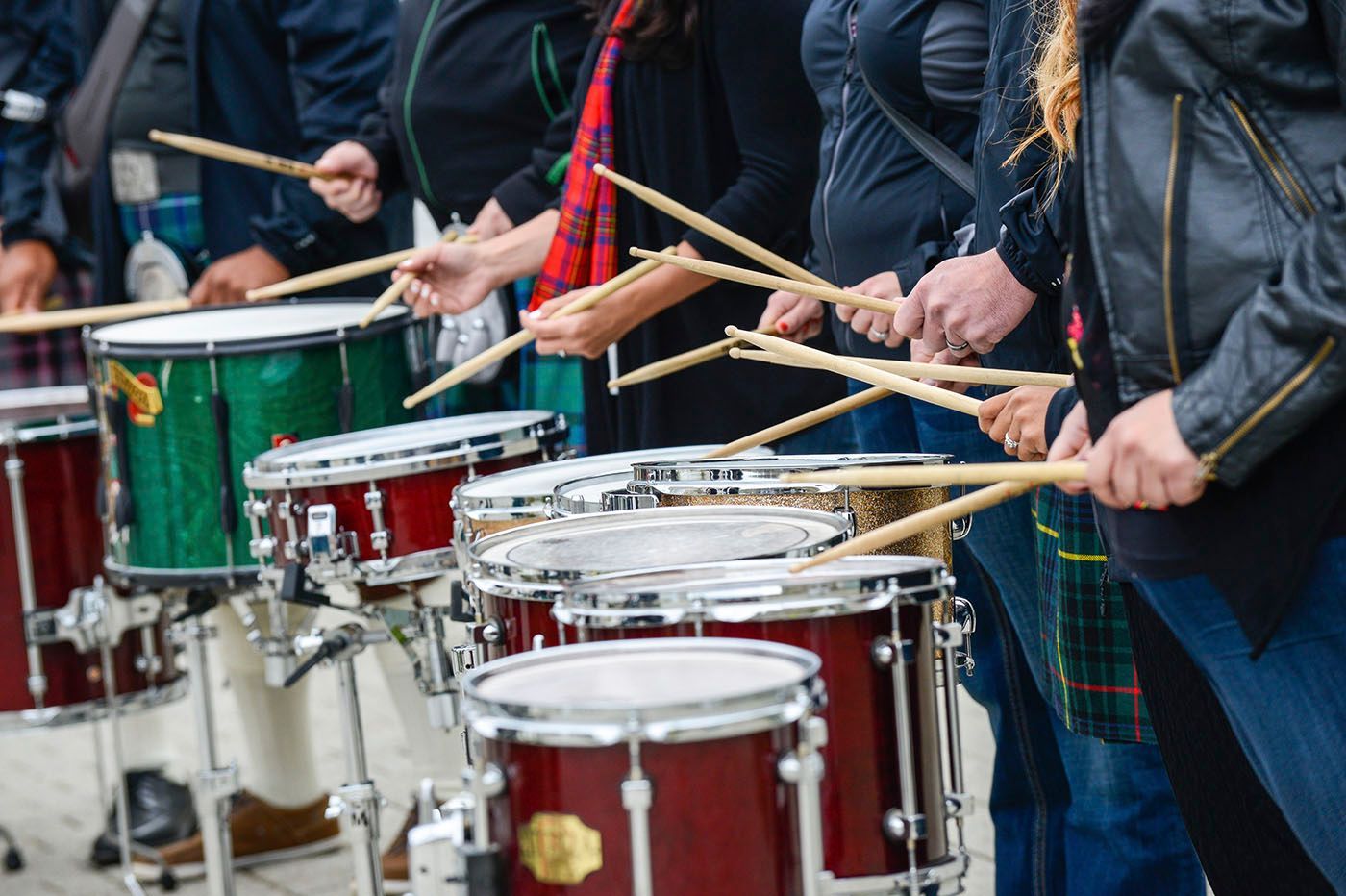 Drummers playing in unison, using drumsticks on a row of snare drums.
