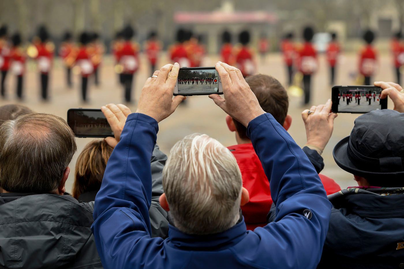 People holding up phones, filming red-coated guards marching in formation.