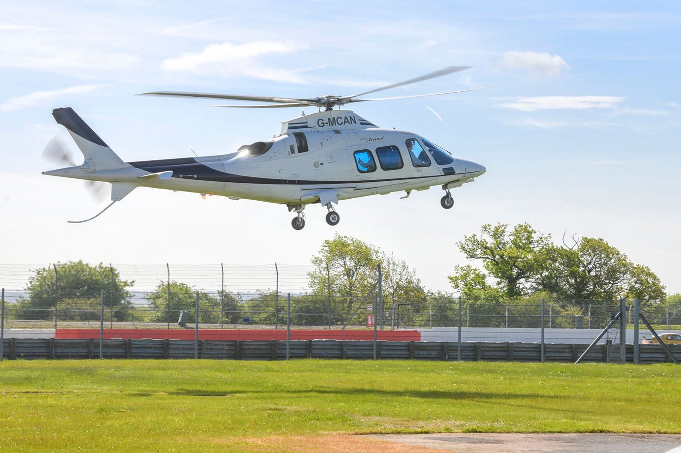 White helicopter taking off from a grass airfield on a sunny day.