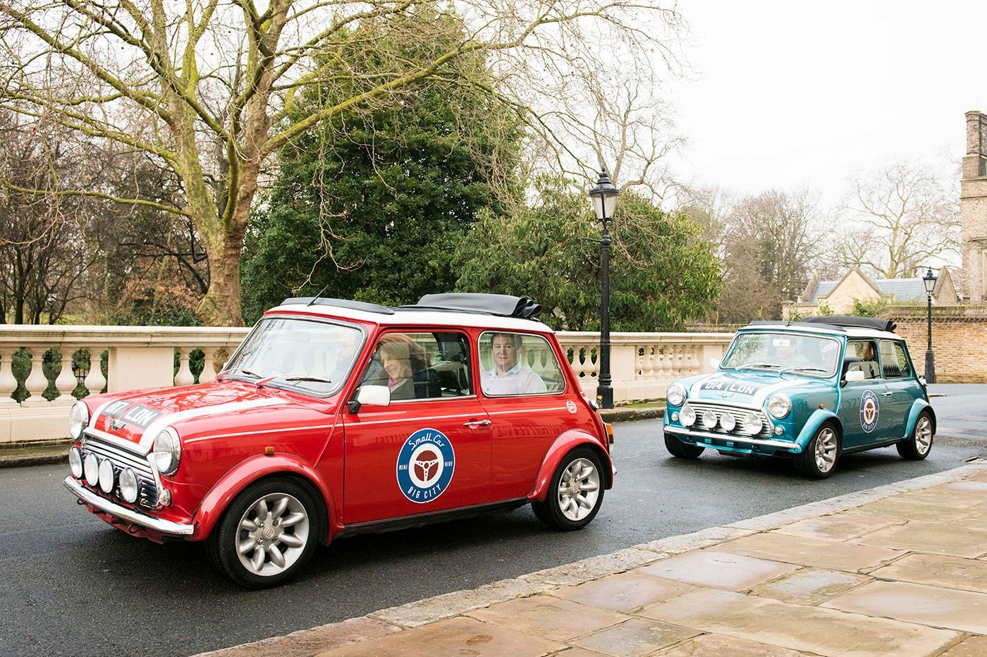 Red and blue vintage Mini Coopers driving on a paved road, possibly a wedding.