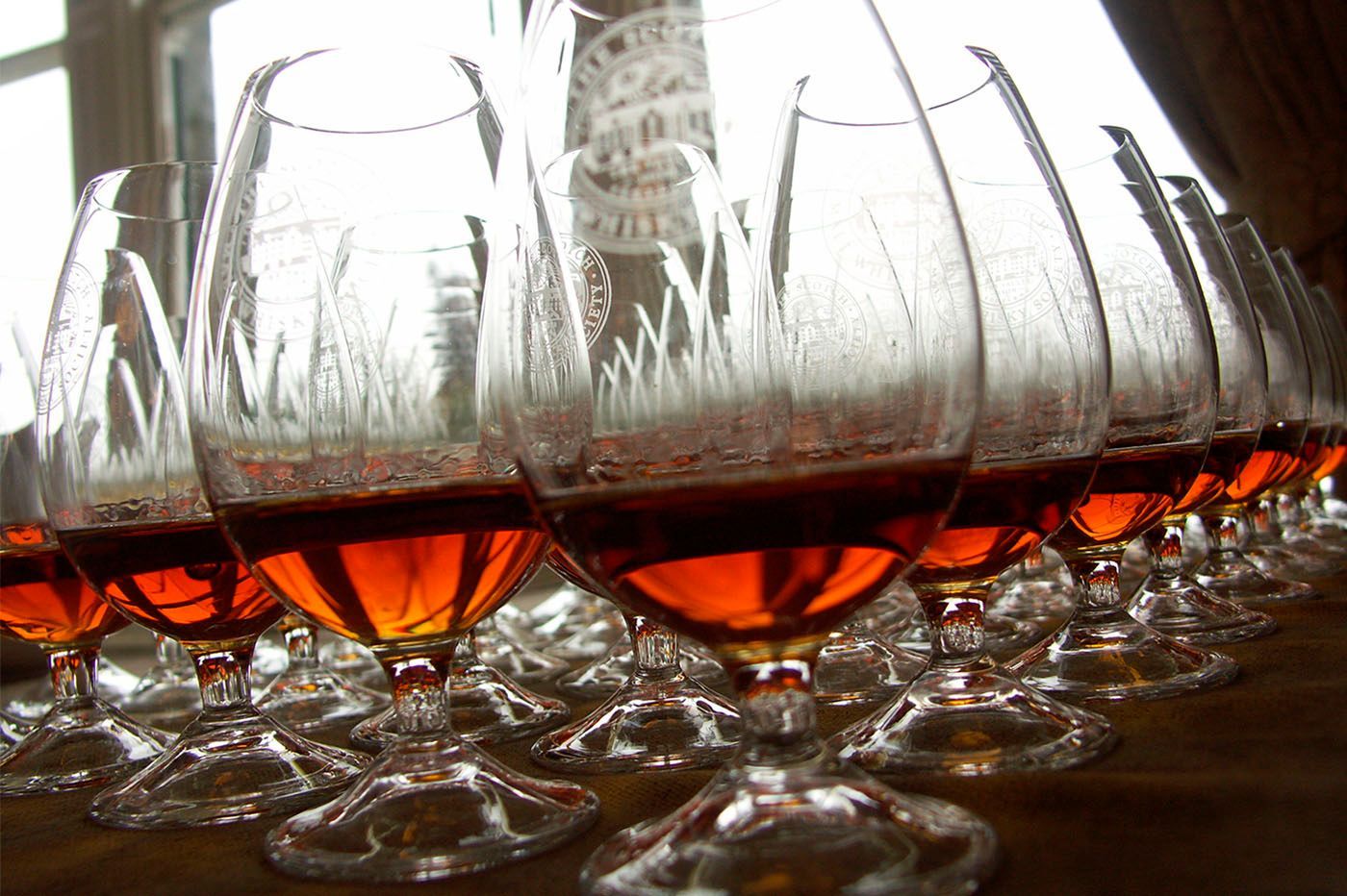 Row of stemmed glasses with amber liquid, etched with grass-like designs.