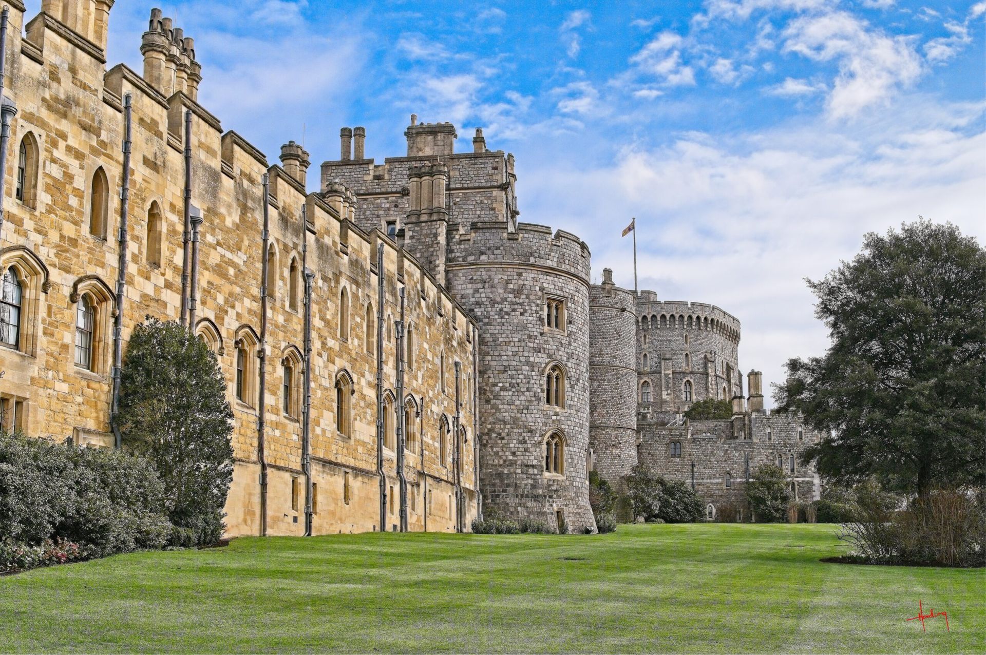 Windsor Castle exterior: stone walls, turrets, and green lawn under a partly cloudy blue sky.