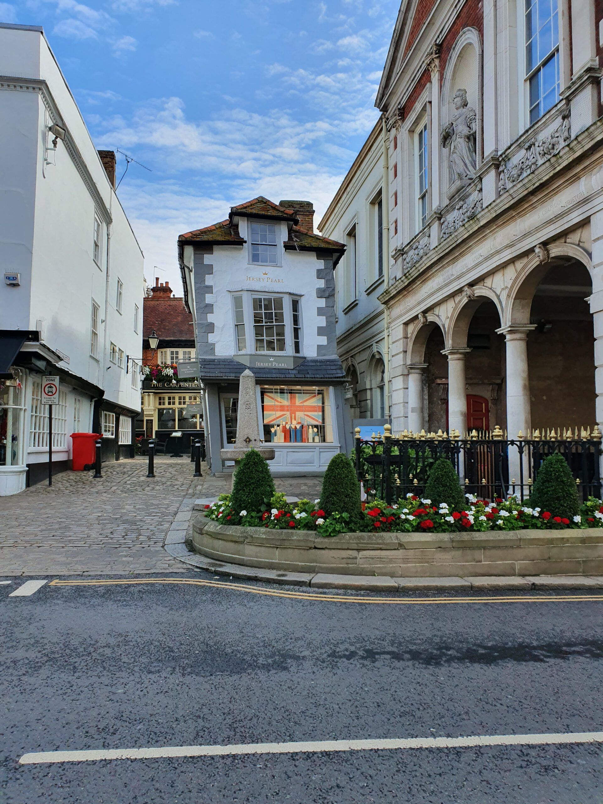 Cobblestone street with old buildings; small, leaning shop, white and ornate buildings on either side.