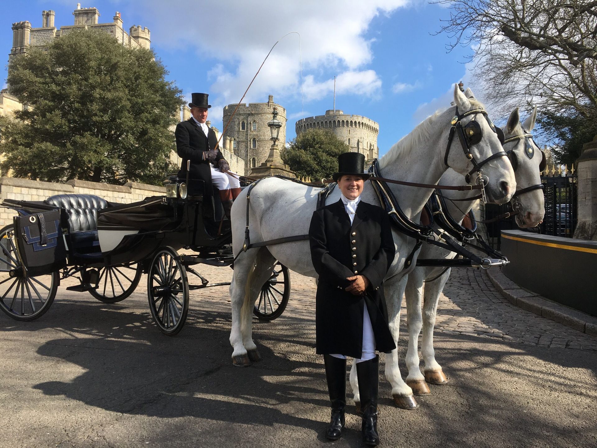 A carriage pulled by two white horses with two people in Windsor Castle setting.