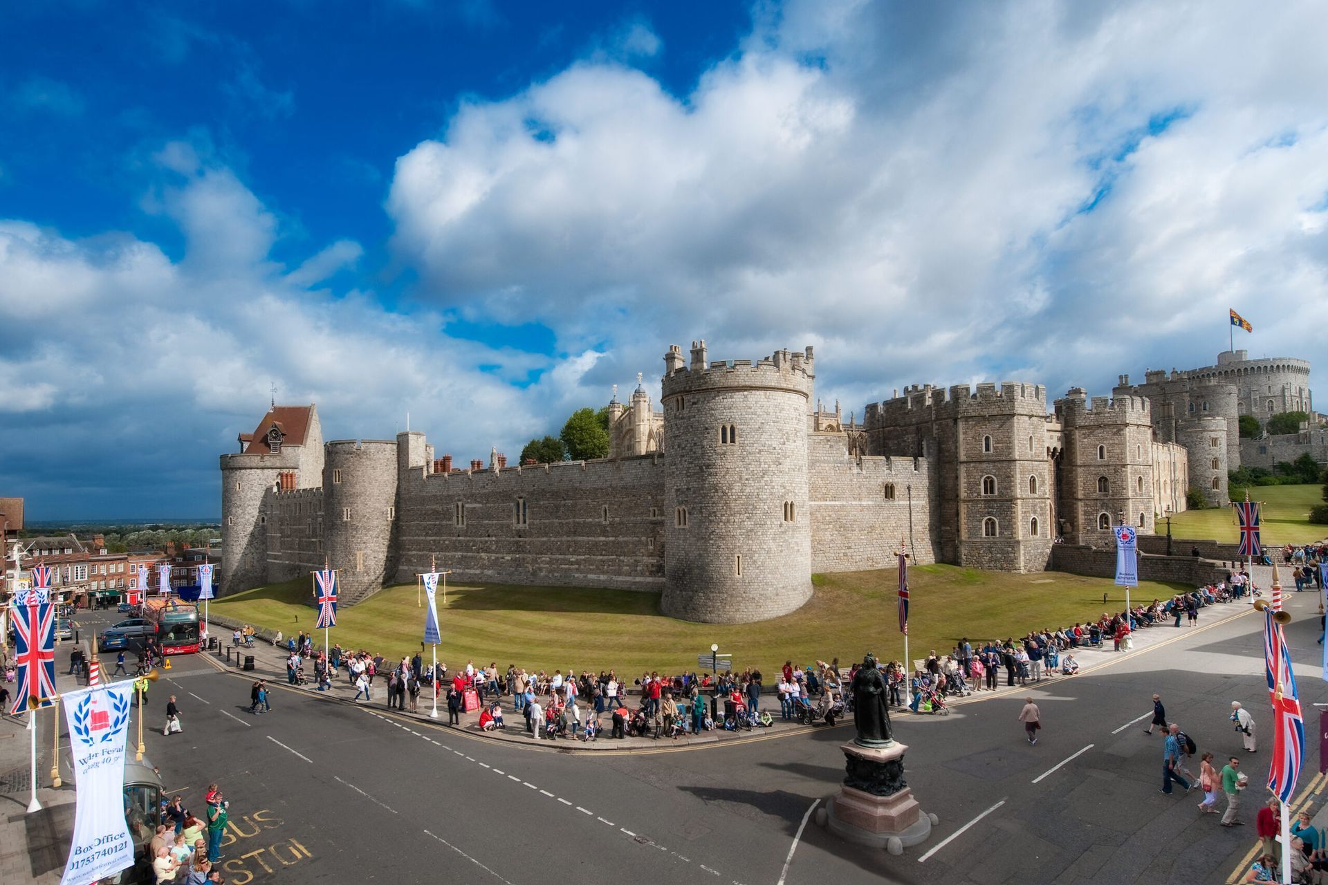 Windsor Castle exterior with crowds, blue sky, and flags.