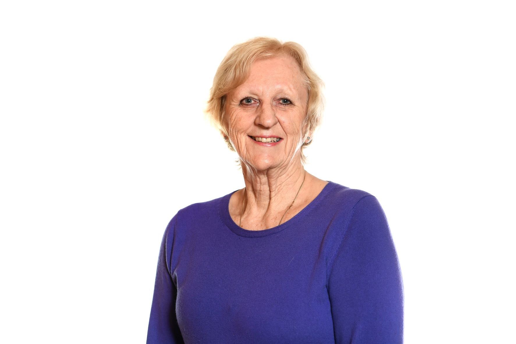 Woman with short blond hair smiling, wearing a blue sweater against a white background.