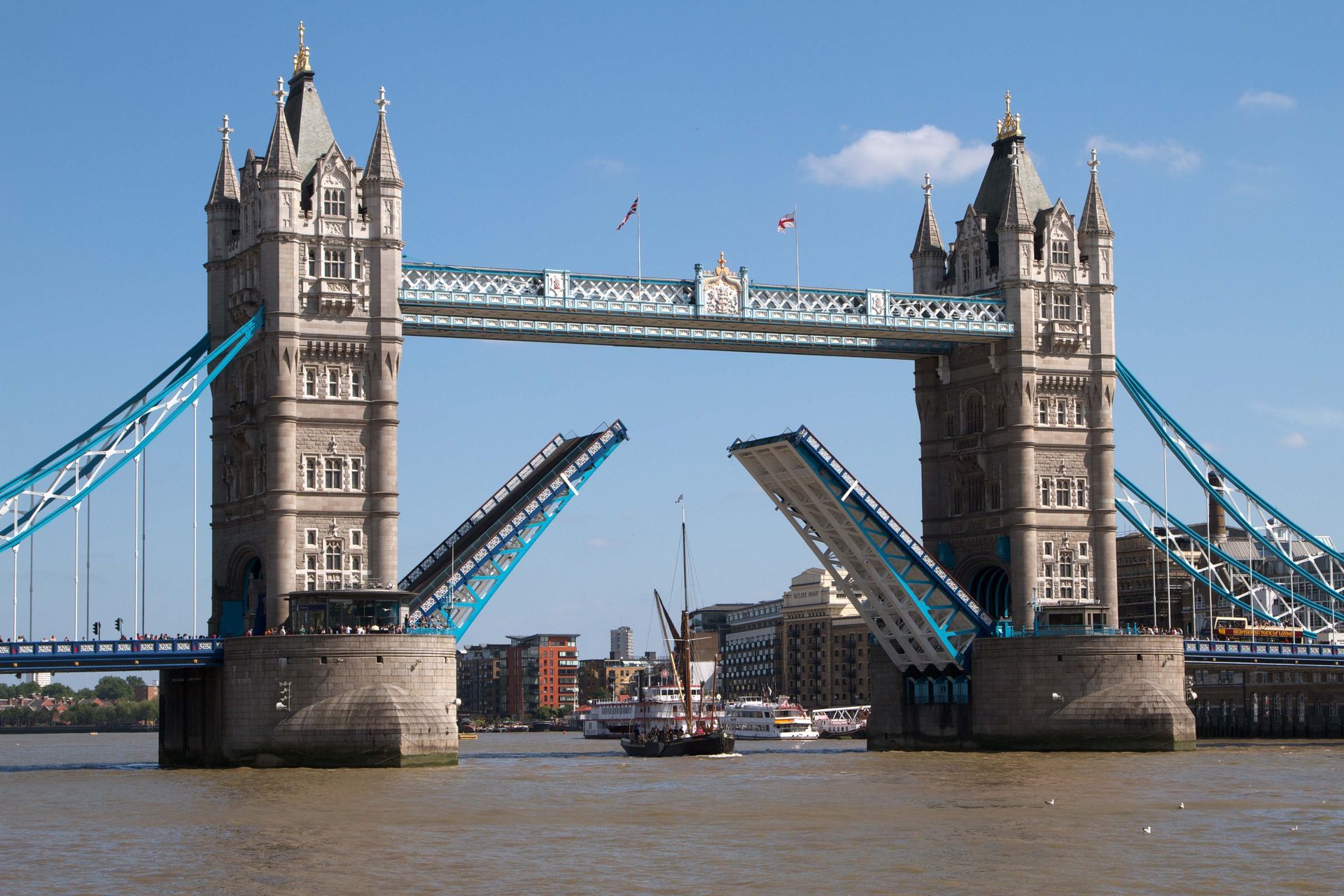Tower Bridge in London, its bascules raised, allowing a boat to pass on the Thames River.
